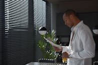 Professional man reads newspaper indoors, holding orange juice, with dramatic morning light.